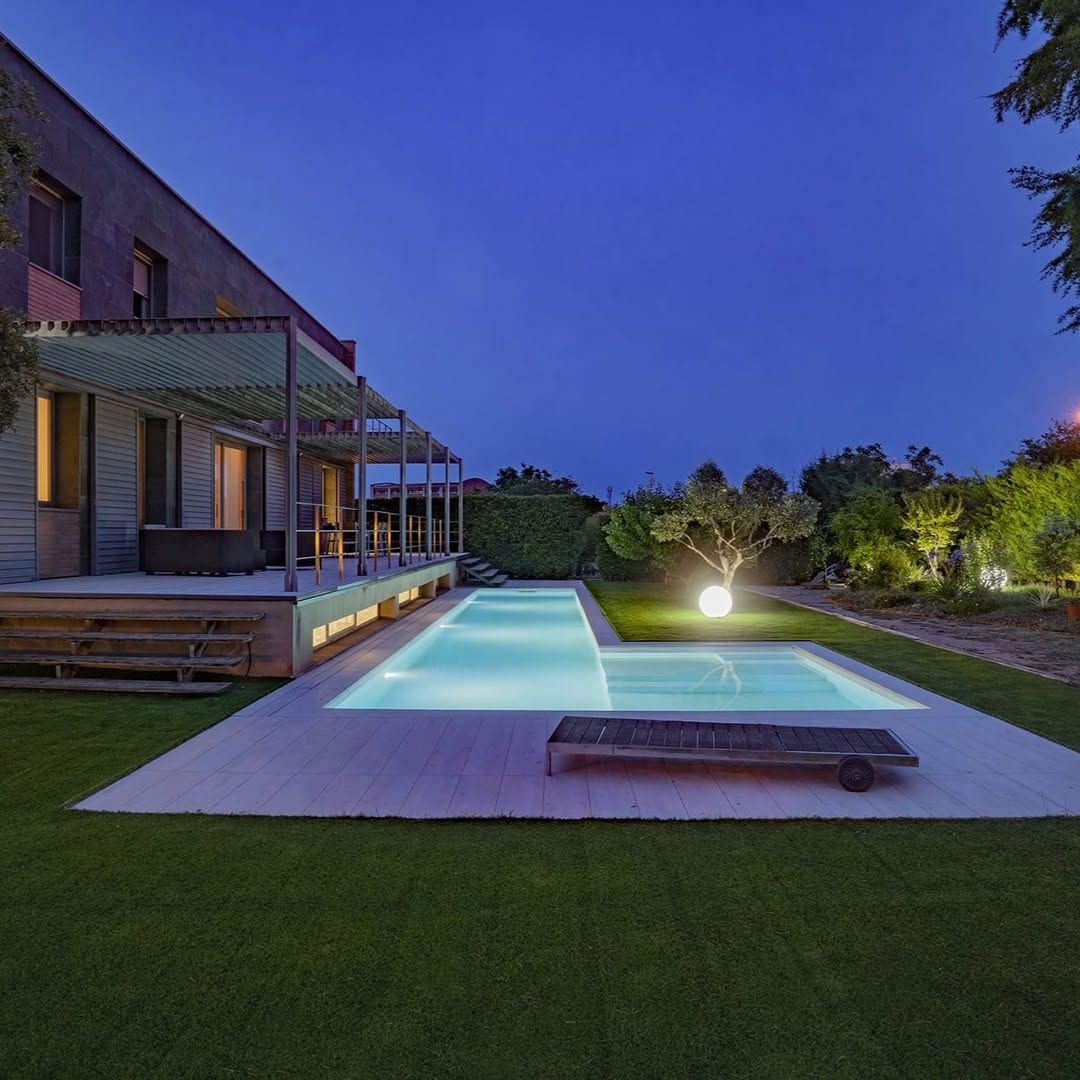 Piscina con terraza Exadeck y jardín al anochecer en Lleida
