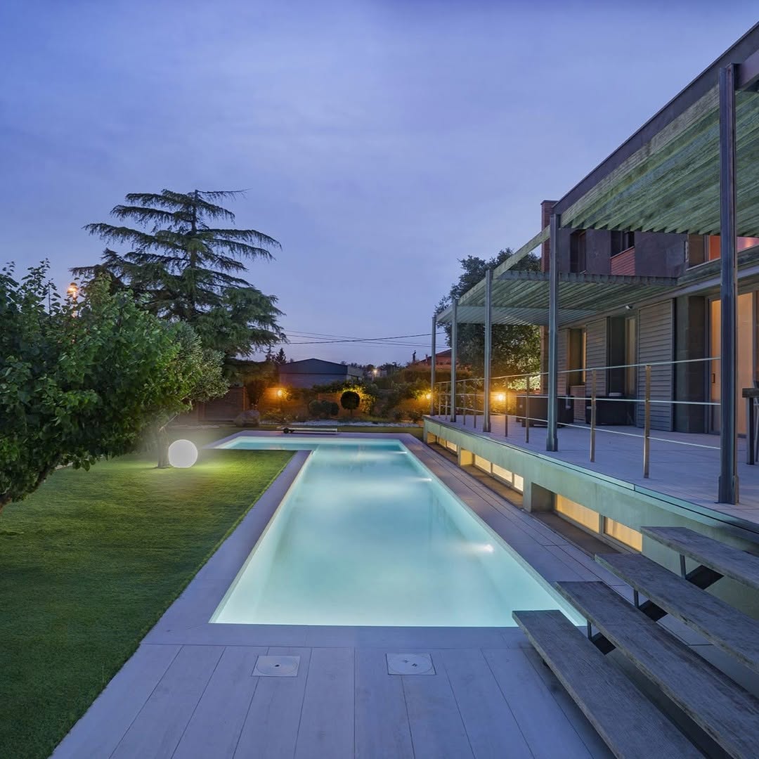 Vista longitudinal de la piscina junto a la fachada de la vivienda